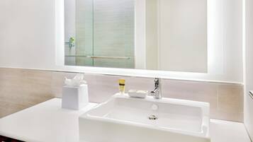 A white bathroom sink with a mirror above it, a glass shower door, and a white towel on the counter.