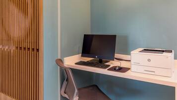A compact office setup with a desktop computer, keyboard, mouse, and HP printer on a white desk against a light blue wall.