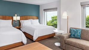 A hotel room with two beds, a sofa, a small round table, and a window with a view of greenery.