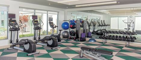 A modern gym with cardio machines, free weights, and a mirrored wall.