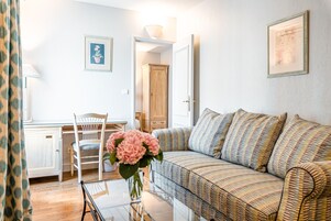 A living room with a sofa, a chair, a table, and a vase with flowers. There is a cabinet and a door in the background.