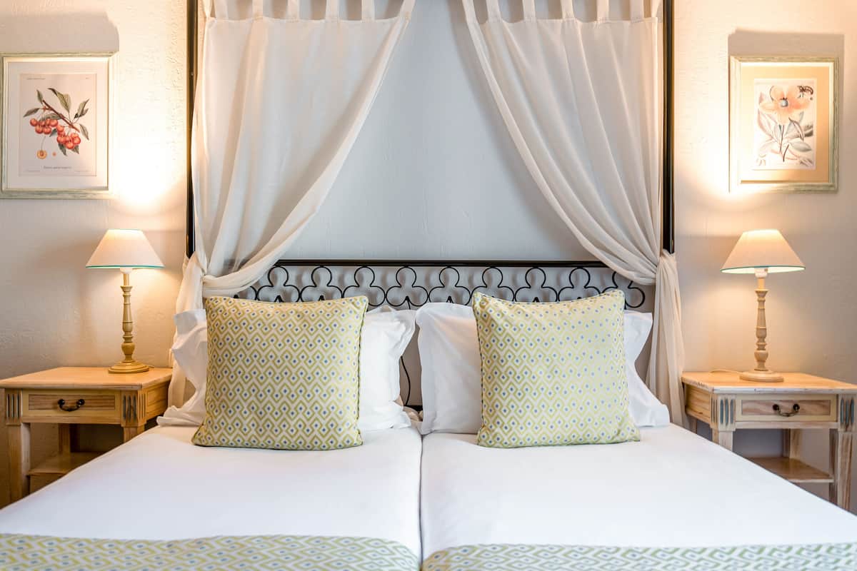 A double bed with a canopy, two bedside tables with lamps, and framed botanical prints on the walls.