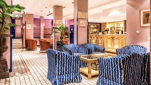 Vestíbulo de hotel con área de bar, asientos con tapicería estampada en azul y una escalera que lleva a otro piso.