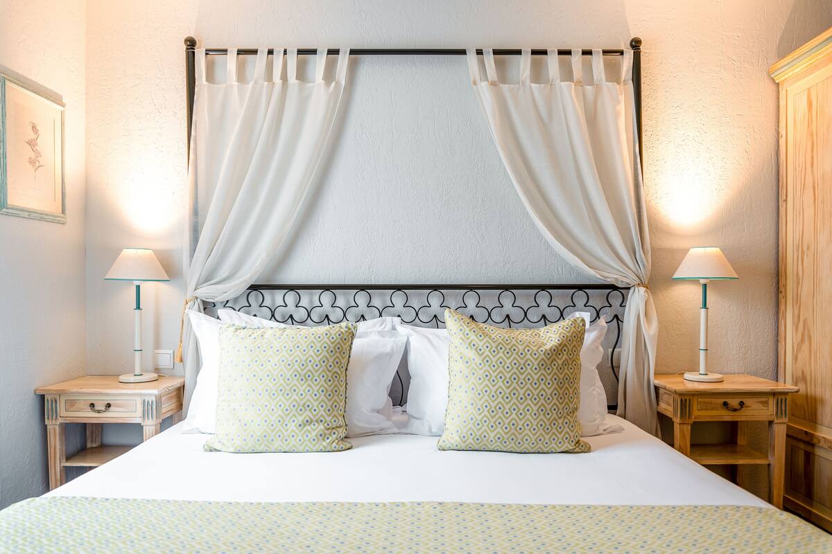 A neatly made bed with patterned bedding, two bedside tables with lamps, and a headboard with curtains.