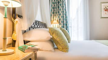 A neatly made bed with patterned pillows, a bedside lamp, and a book on a wooden nightstand.