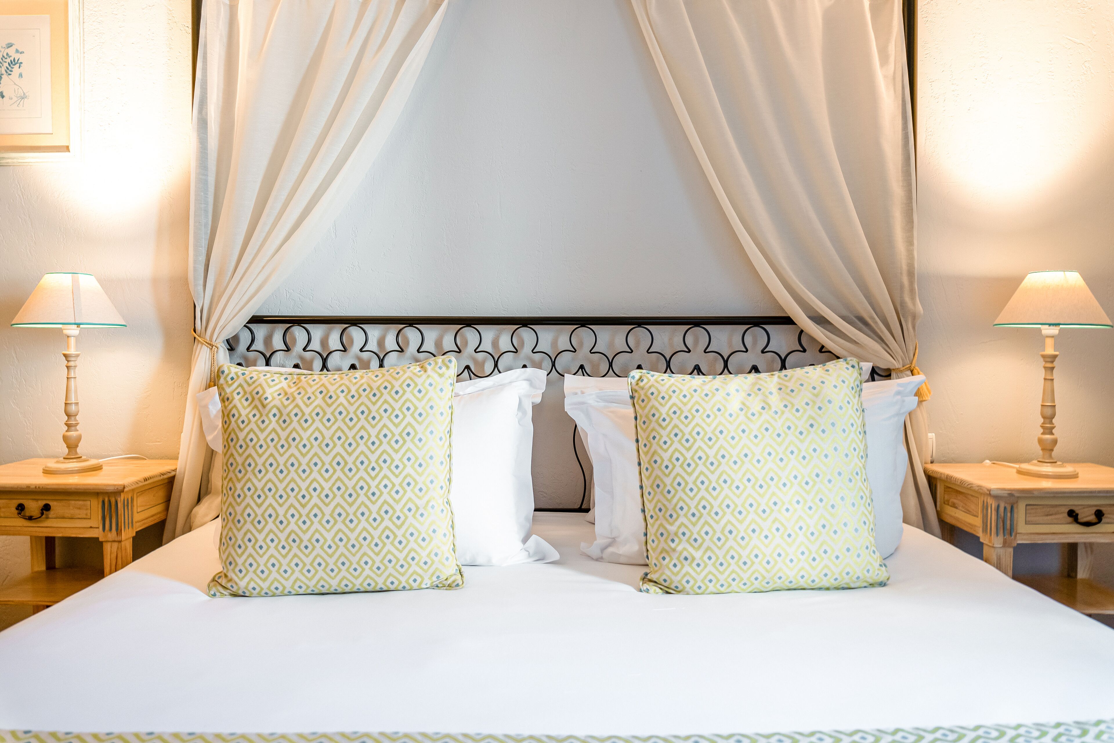 Una cama con dosel impecablemente arreglada, dos mesitas de noche con lámparas y almohadas estampadas.