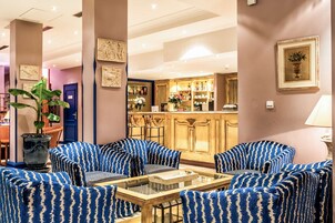 A lobby with blue patterned sofas, a glass coffee table, a bar area, and a potted plant.