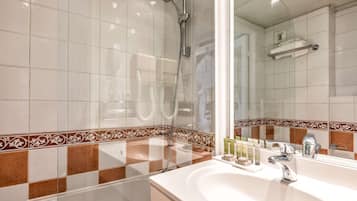 A bathroom with a large mirror, a shower, and a sink with toiletries.
