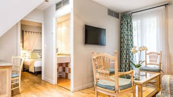 A modern hotel room with a wooden floor, a dining area with a glass table, and a TV mounted on the wall.