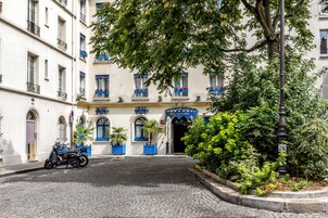 Une rue pavée menant à un bâtiment aux fenêtres et balcons encadrés de bleu.