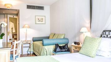 A hotel room with a bed, two bedside tables, a chair, a desk, a lamp, a picture frame, and a bathroom visible through an open door.