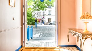 Entrada de un hotel con vista a la calle, toldo azul y una lámpara de mesa.