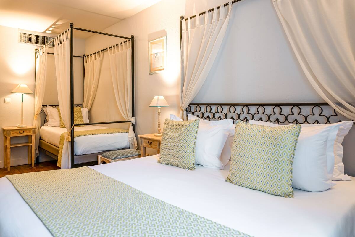 A four-poster canopy bed with a patterned bedspread, two bedside tables with lamps, and a mirror on the wall.
