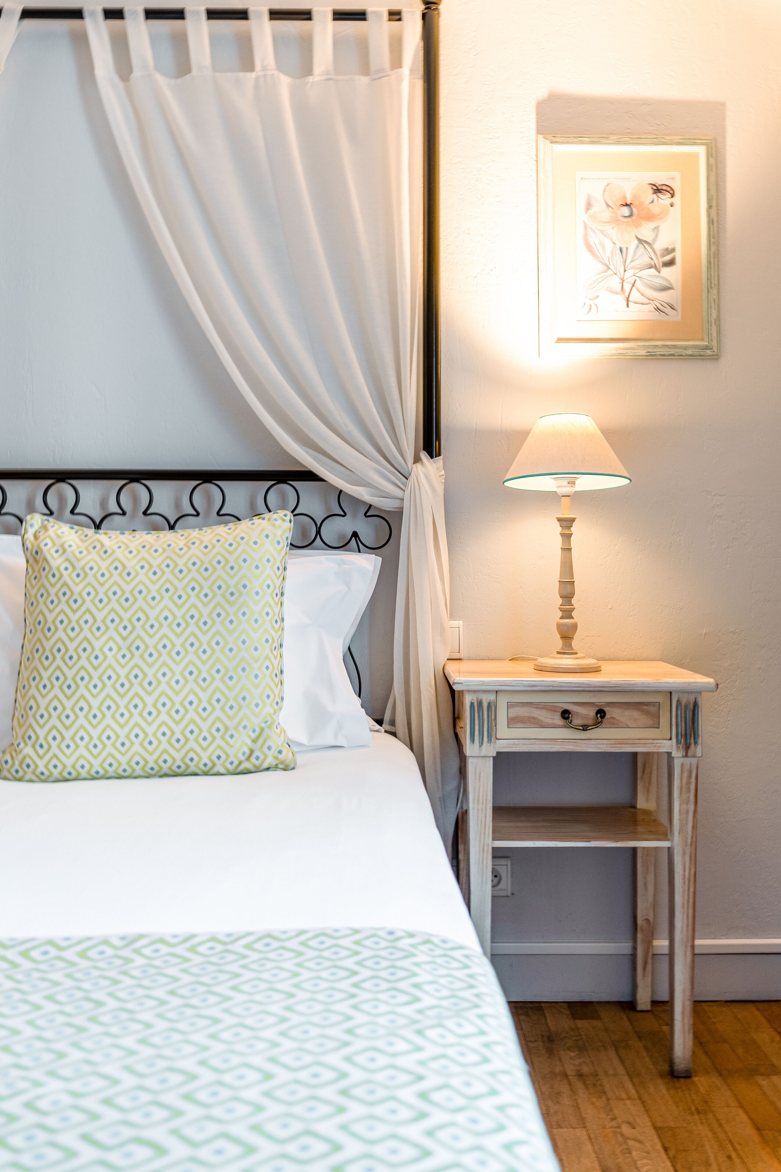 A neatly made bed with patterned bedding, a bedside table with a lamp, and a framed artwork on the wall.
