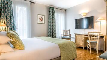 Habitación de hotel con cama, escritorio, silla, televisión y un cuadro en la pared.