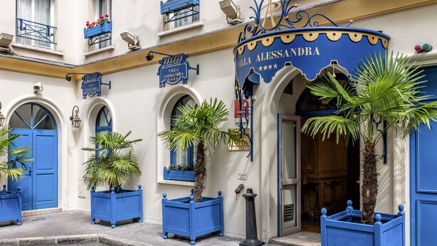 Un edificio con fachada azul, un letrero que dice "Villa Alessandra" y plantas en macetas.