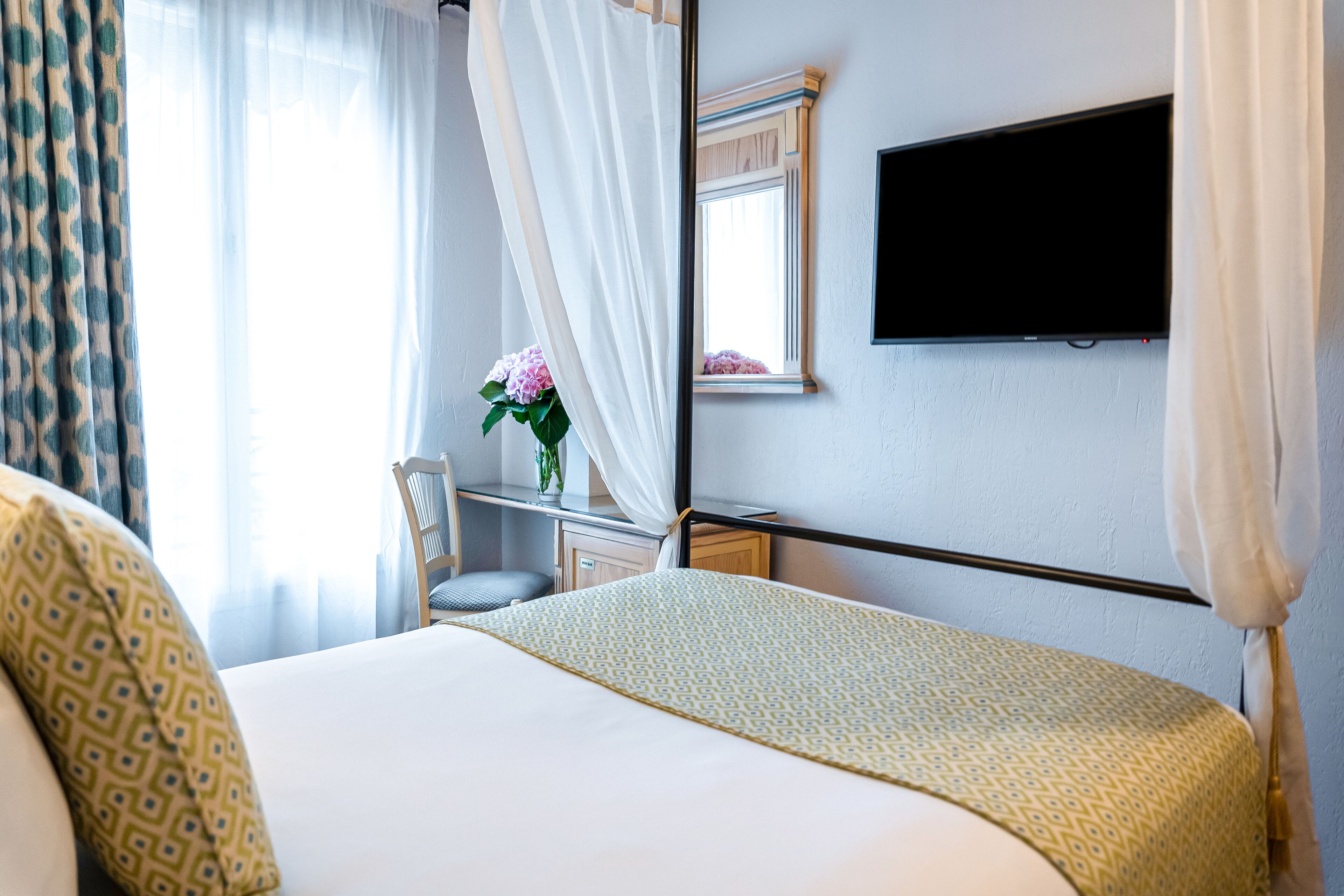 A hotel room with a bed, a desk, a chair, a TV, and a window with curtains.