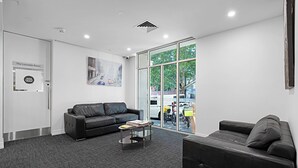 Un espacio de oficina moderno con un sofá de cuero negro, una mesa de centro de vidrio y un ventanal con vistas al exterior.