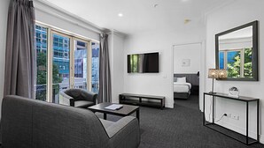 Habitación de hotel con sofá, una mesita, televisión, mesita de noche, espejo y ventana con cortinas.