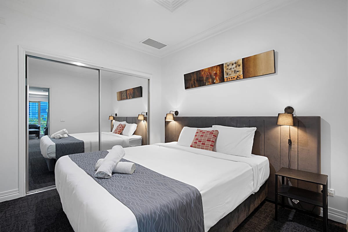 A hotel room with a large bed, a bedside table, a mirror, and artwork on the wall.