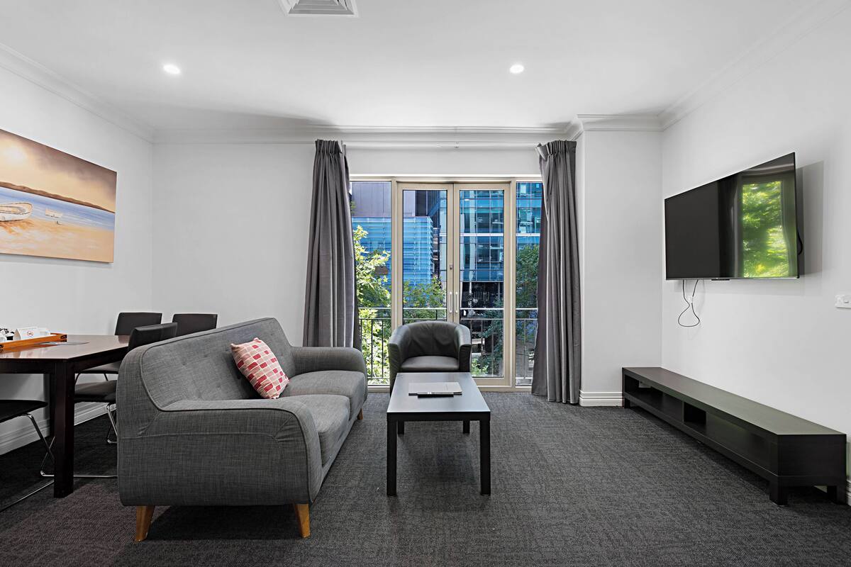 A modern living room with a sofa, a coffee table, a TV, and a balcony with a city view.