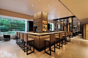 A modern bar area with a central island, bar stools, and a view of a garden through large windows.