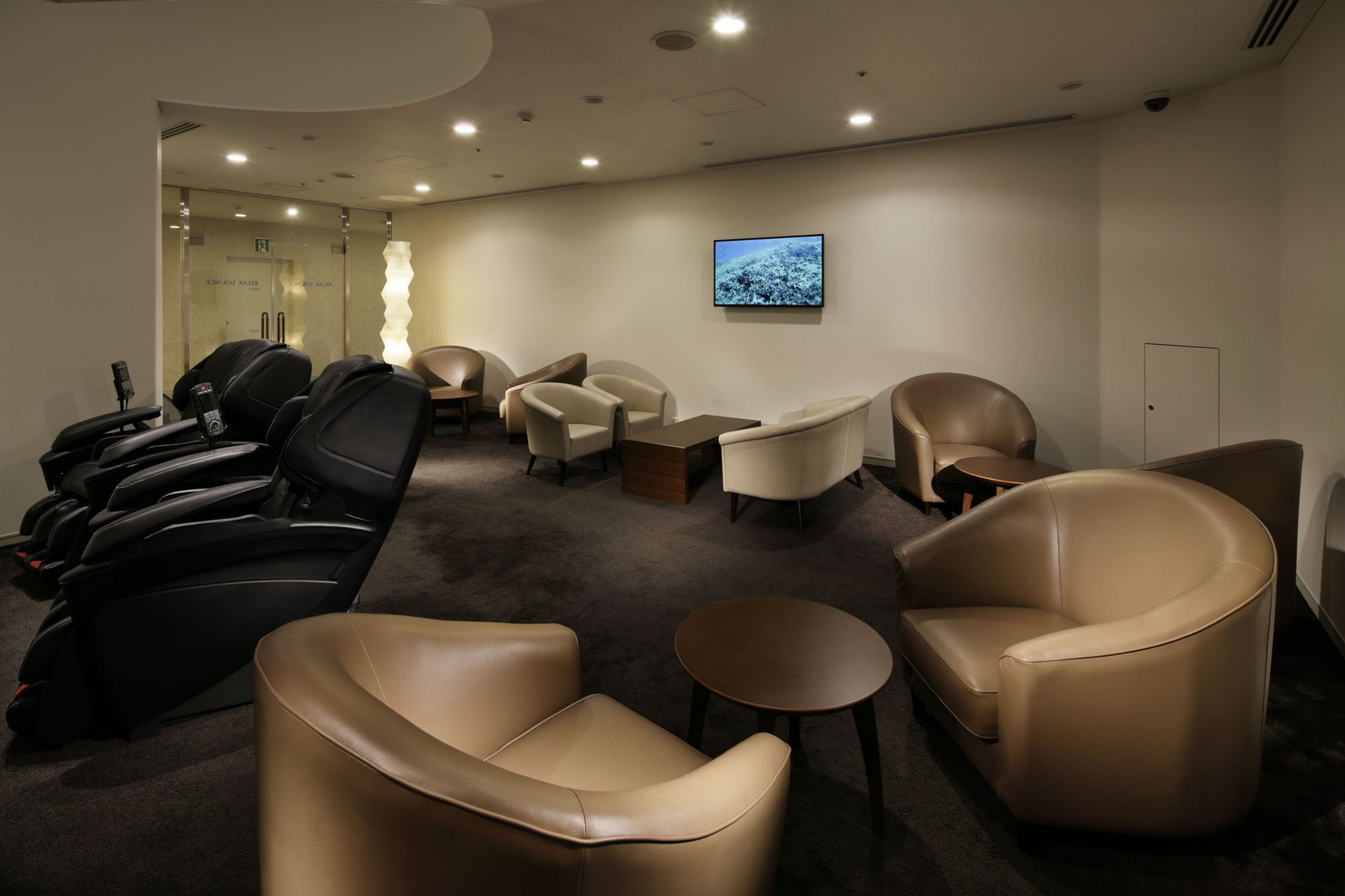 A massage therapy room with multiple massage chairs, a small table, and a wall-mounted television.