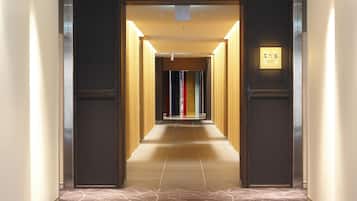 Un couloir d’hôtel moderne, avec un long passage rectiligne menant à une porte.