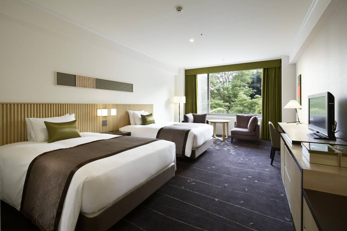 A hotel room with two beds, a desk, a television, and a window with curtains.
