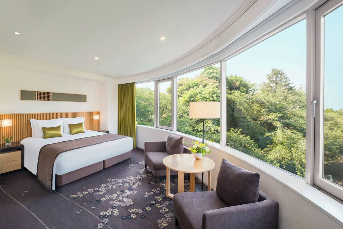 A modern hotel room with a large bed, a seating area, and a view of the outdoors.