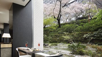 Une chambre d’hôtel moderne avec un coin repas donnant sur un bassin à carpes koï et des cerisiers en fleurs.