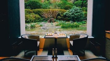 Een eethoek met een tafel en stoelen, met uitzicht op een tuin met verschillende planten en een klein vijvertje.