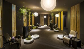 A modern, dimly lit lounge area with a central seating arrangement, ambient lighting, and vertical bamboo panels on the walls.