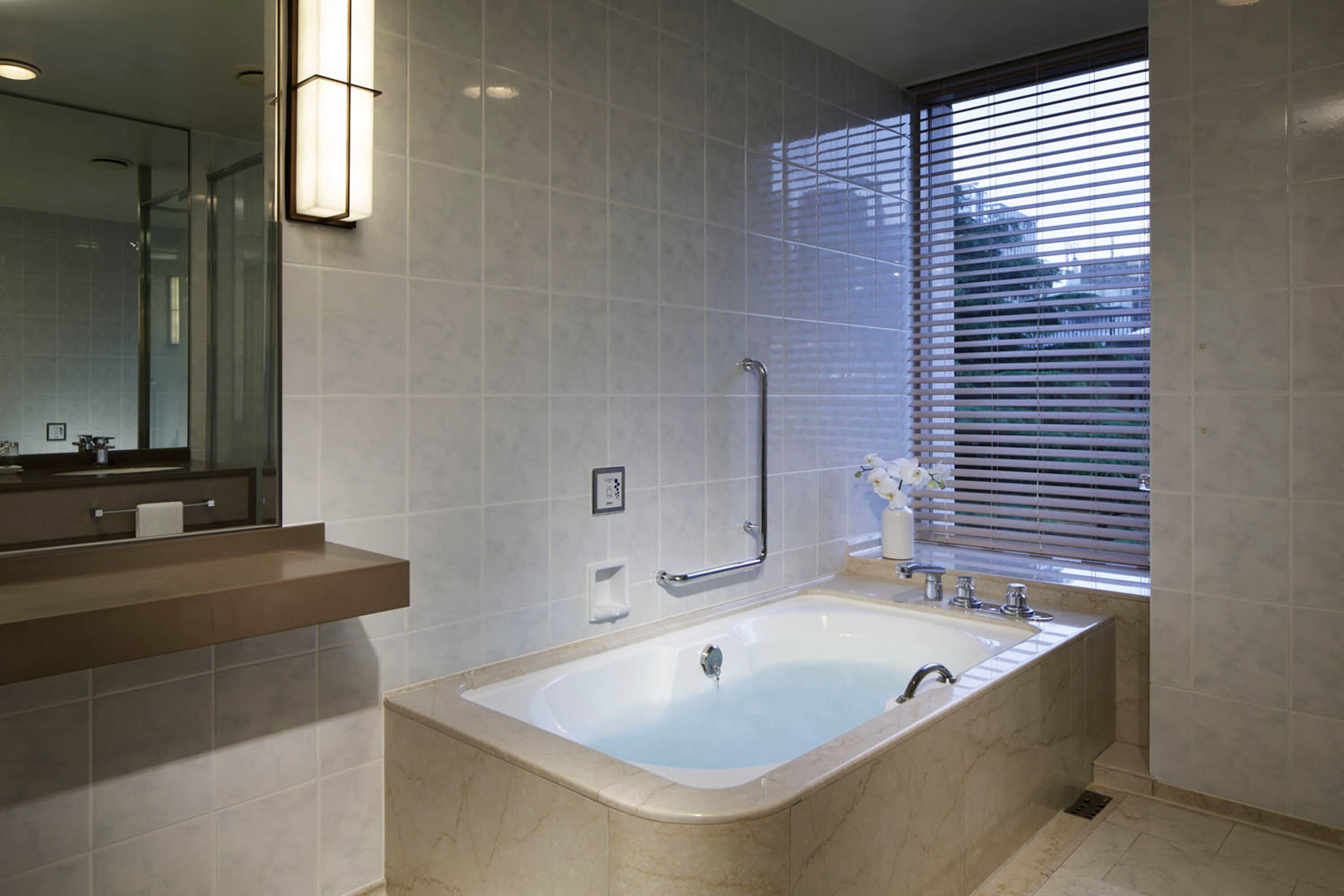 Un baño moderno con una bañera grande, un tocador con espejo y una ventana con persianas.