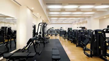 A gym with various exercise machines, mirrors, and a wooden floor.