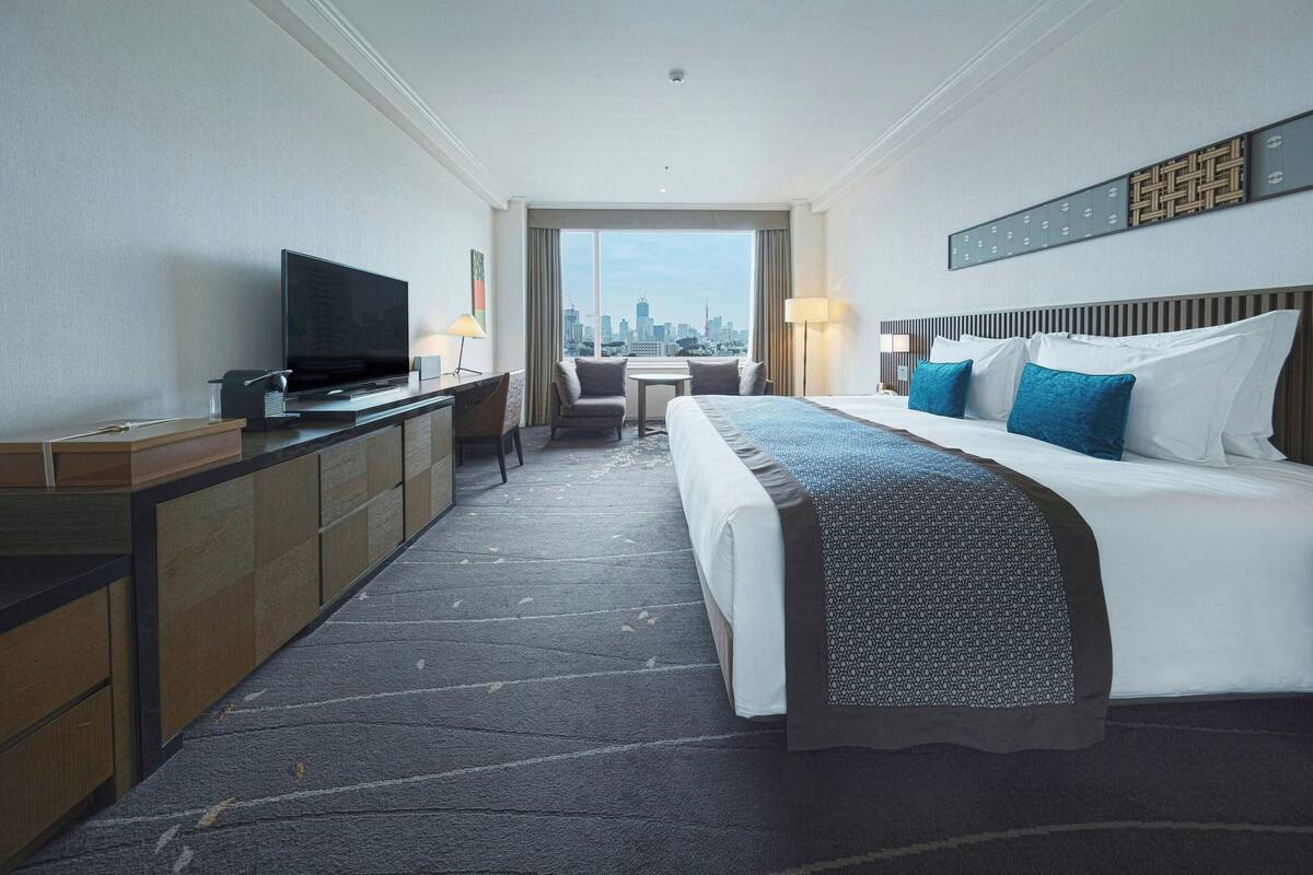 A hotel room with a bed, a TV, a desk, and a view of the city skyline.
