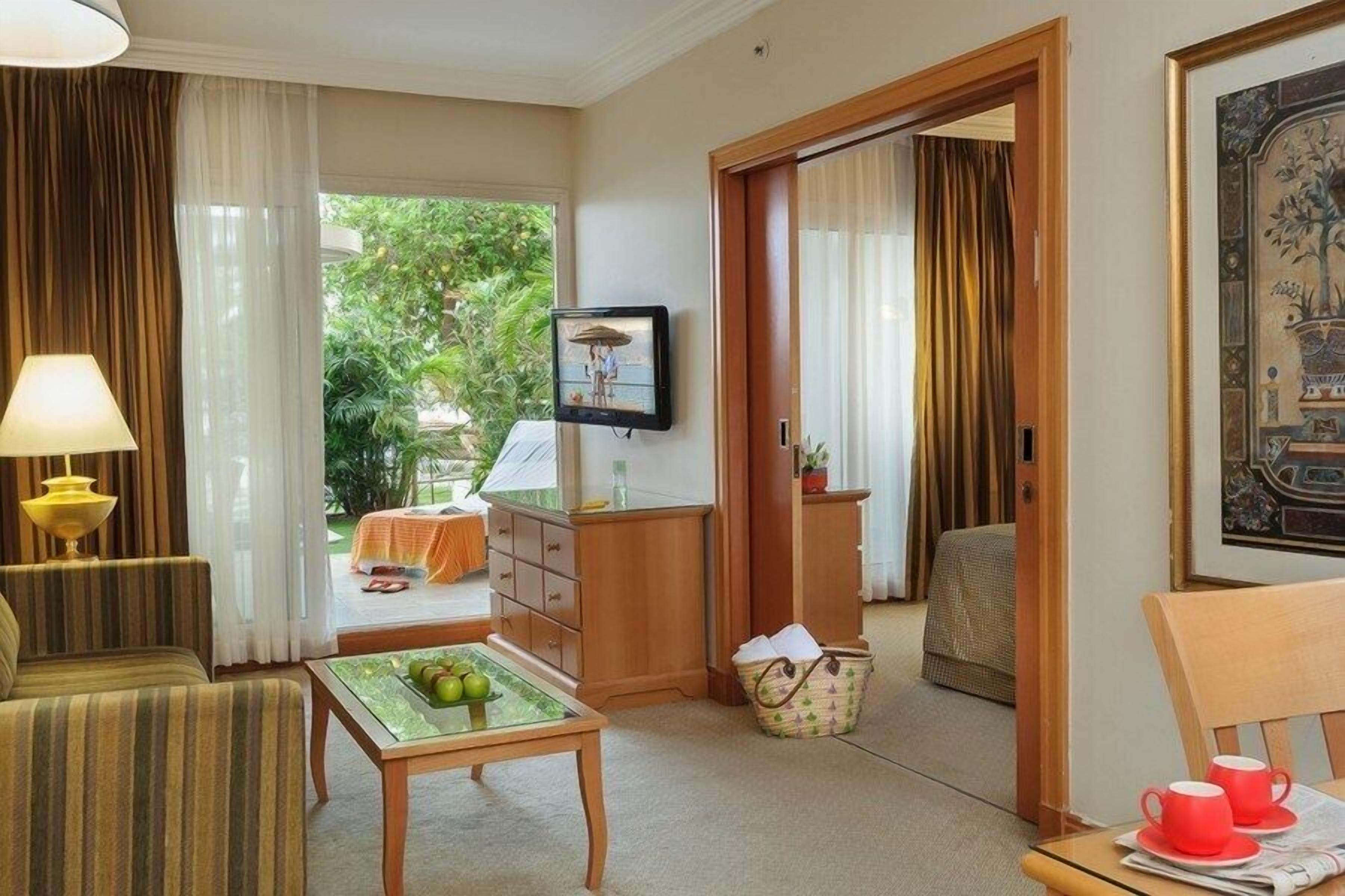 A hotel room with a sofa, a table with fruit, a television, and a painting.