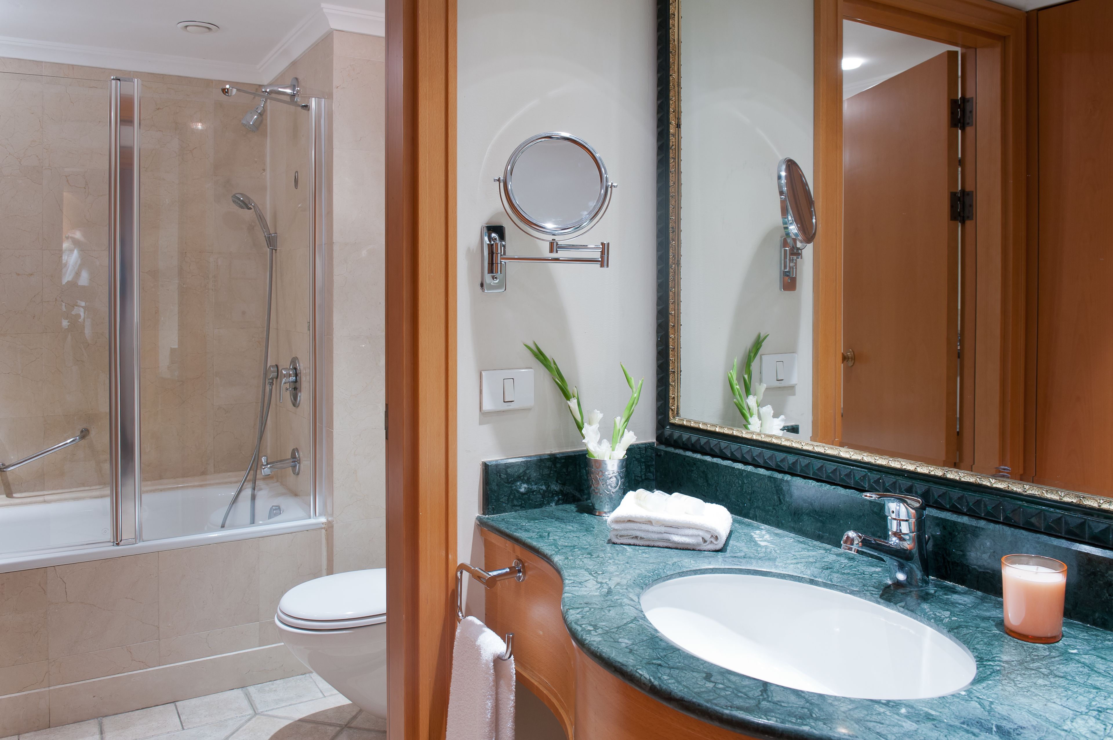 A modern bathroom with a glass-enclosed shower, a large mirror, and a marble countertop.