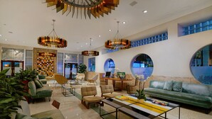 A spacious lobby with modern furniture, including sofas and armchairs, a coffee table, and a large round mirror. There are multiple ceiling lights and a decorative chandelier. - The Tony Hotel South Beach (Miami Beach)