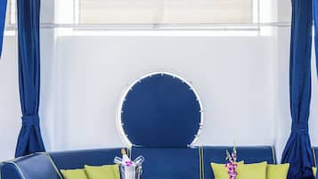 A modern, nautical-themed seating area with a blue sofa, green cushions, and a round mirror.