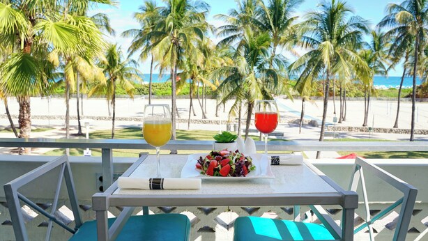 A table with a plate of food and two drinks, overlooking a beach with palm trees. - The Tony Hotel South Beach (Miami Beach)