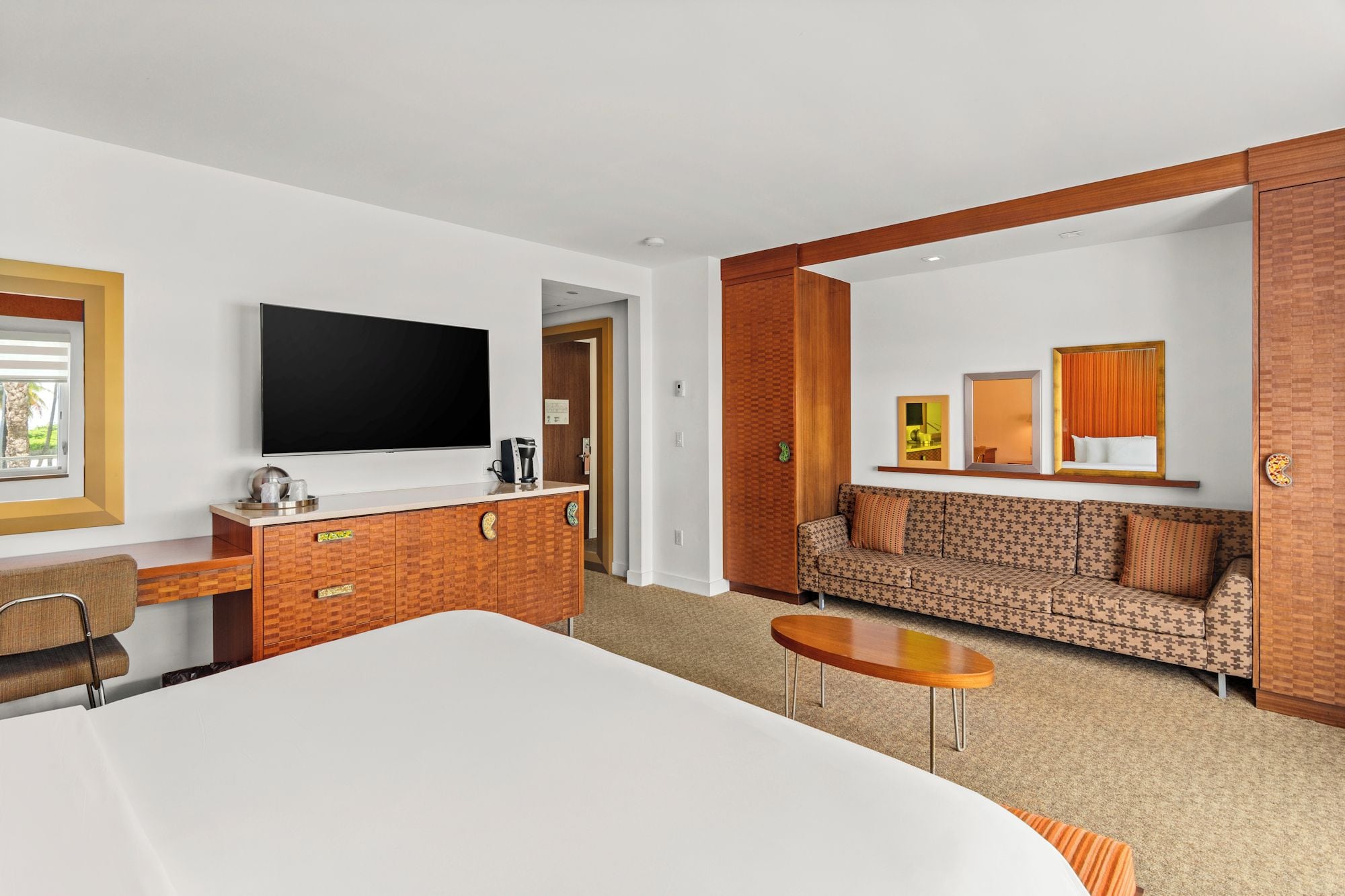 A hotel room with a large bed, a desk, a television, a sofa, and a small table.