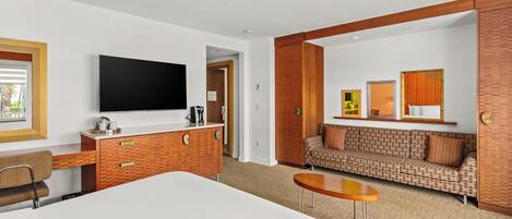 A hotel room with a large bed, a desk, a television, a sofa, and a small table.