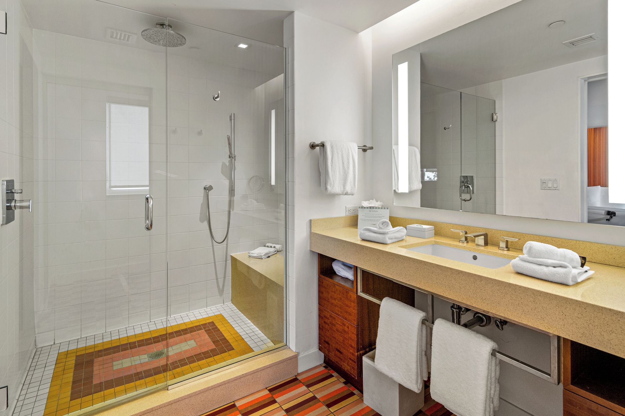 A modern bathroom with a glass-enclosed shower, a vanity with a sink and mirror, and a patterned floor.
