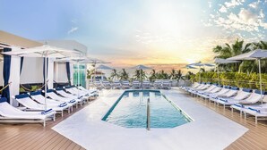A pool area with sun loungers and umbrellas, surrounded by palm trees and a clear sky. - The Tony Hotel South Beach (Miami Beach)