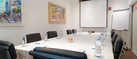 Una sala de conferencias con una larga mesa, botellas de agua y una pantalla de proyector.