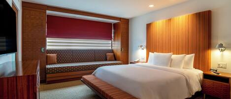 A hotel room with a large bed, a bench, a desk, and a TV.