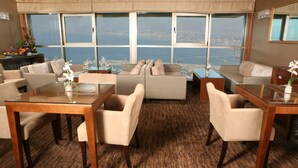 Ampla sala de estar com uma grande janela que oferece vista da cidade, uma mesa de centro de vidro e assentos confortáveis.
