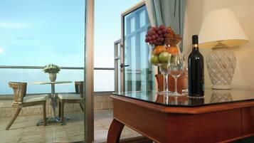 Un balcon avec une table, des chaises, un vase de fleurs, un panier de fruits, des verres à vin, une bouteille de vin et une lampe.