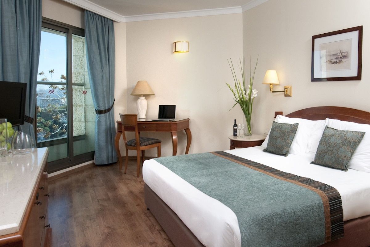 A hotel room with a bed, desk, chair, and a window with curtains.